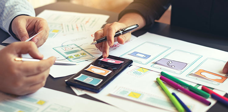 de handen van twee mijnsen werken aan een creatieve opdracht met papier, pennen en stiften